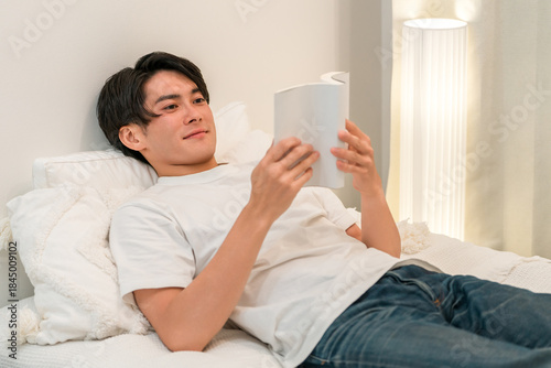 Young Asian man reading a book while lying in bed