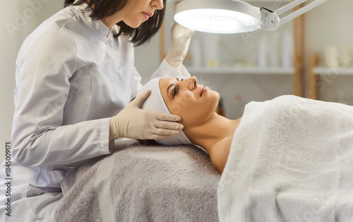 Cosmetologist, dermatologist doing female facial treatment in spa salon, professional magnifying lamp examining skin, medical problems, individual conditions, dermatological disease, full examination 