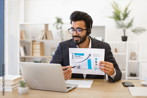 An Indian businessman presents financial data during a video conference, using a laptop and headset