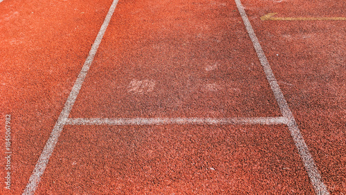 Close up shot of a red running track with white lane lines, suggesting competition, speed, and dedication