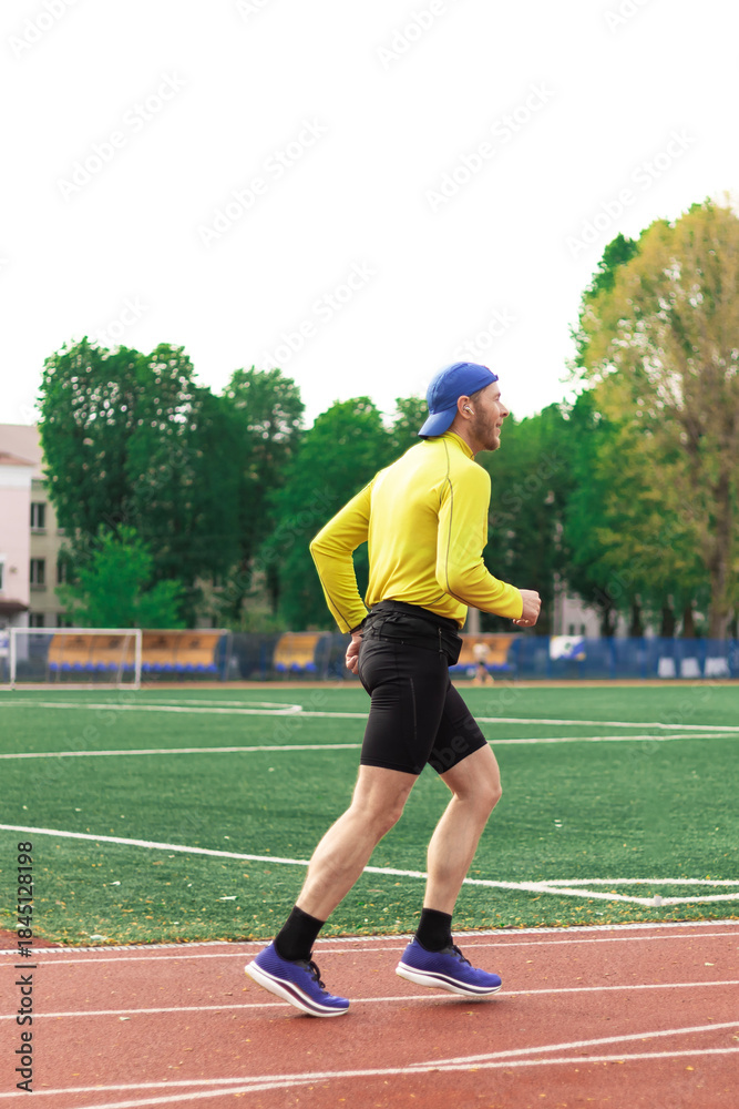 Obraz premium A man wearing a backwards cap runs on a stadium track