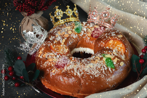Roscon de reyes on a red plate with a red berries branches and crowns of the wise men. Kings day concept spanish three kings cake