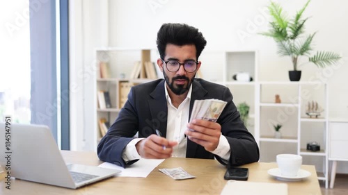 An Indian businessman is working on finances while holding a stack of cash in his office