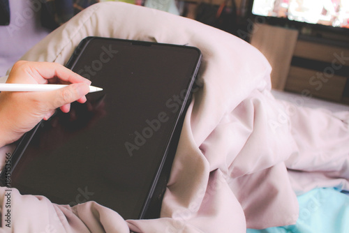 Close up of hand using stylus pen on tablet screen while lying on bed, digital lifestyle at home.