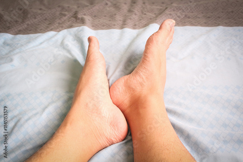 Close up of male feet on blue and white bedsheets, relaxing at home during weekend.