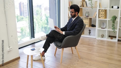 An Arab businessman is working on his laptop while sitting in a modern office, looking out the window