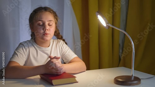 Child places hands gently on bible in silent prayer. Bible open in front of child. Worship moment held in stillness. Child keeps hands folded. Worship scene unfolds near bible gentle evening peace.