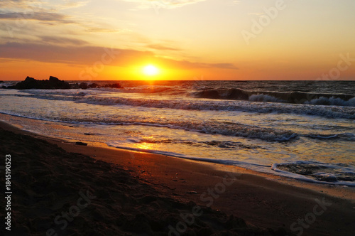 Sunrise on the seashore with waves on a warm summer morning