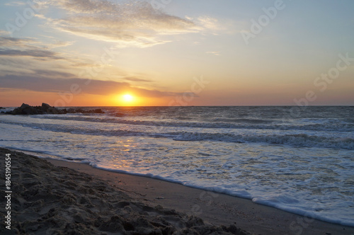 Sunrise on the seashore with waves on a warm summer morning
