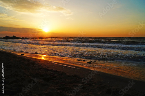 Sunrise on the seashore with waves on a warm summer morning