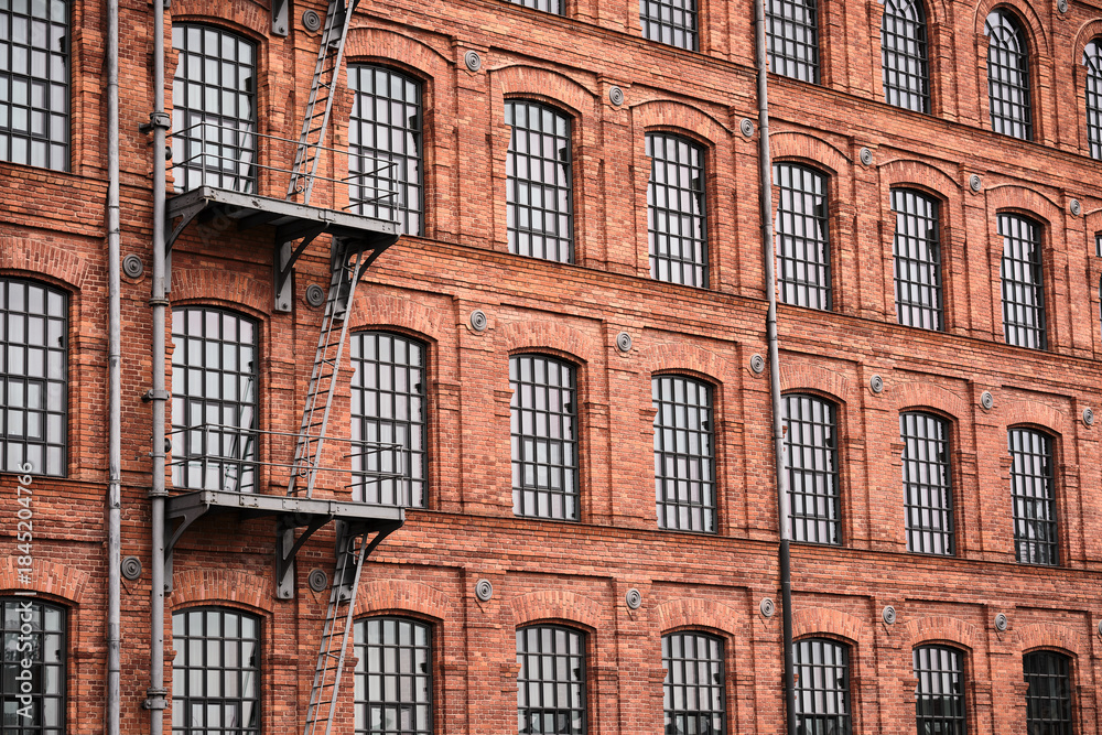 Fototapeta premium Panoramic red brick factory facade with repeating tall windows, an industrial architectural background suitable for web, real estate or business design.