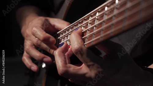 Close up of finger tapping bass of musician at the bass guitar , musician playing bass guitar in the room and with spotlights ,Bassist practicing in a  studio.