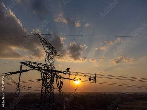 Aerial view of silhouettes of workers atop a towering transmission tower against a vibrant sunset, Joypurhat, Rajshahi Division, Bangladesh.