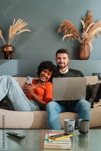 Joyful couple sharing moments together as they use their smartphone and laptop, capturing the essence of modern companionship and technology in their cozy living space.