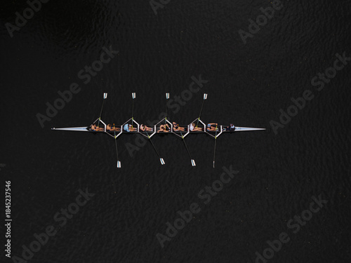 Aerial view of a rowing team gliding across the Charles River's dark waters, their oars creating subtle ripples, Boston, Massachusetts, United States.