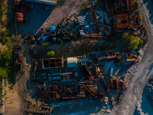 Aerial view of a cluttered junkyard filled with rusty metal debris, old tires, and discarded materials creating a stark contrast against the green patches, Boston, Massachusetts, United States.