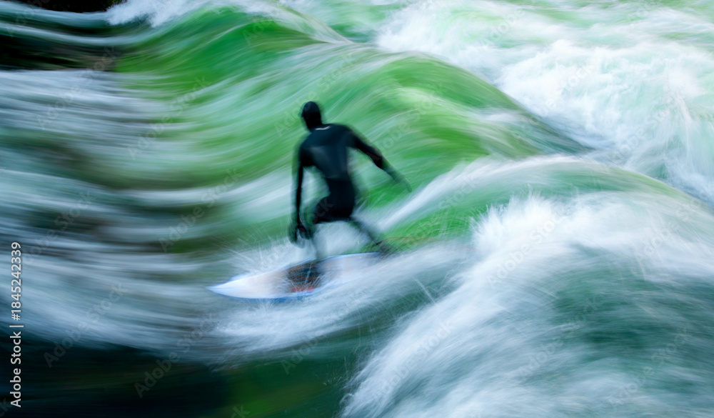 Fototapeta premium Silhouette of a surfer in a dark wetsuit surfing a standing wave on the Eisbach in Munich (Bavaria). Motion blur caused by long exposure and the flow of the water. Outdoor sport in a park in Germany.