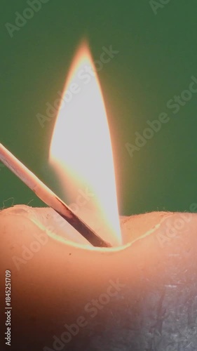 Lighting a match to ignite a candle on a dark surface with a green background seen in close-up