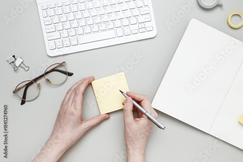 Woman writing on sticky note at organized workspace with notebook and stationery items