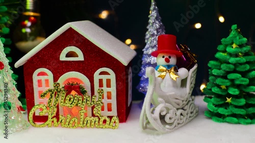 On a dark blue background with flashing lights there are many Christmas trees and a red house with letters and a snowman on a sled