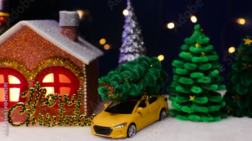 On a dark blue background with flashing lights there are many Christmas trees and a brown house with letters and a yellow car