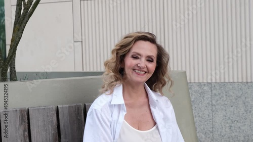 A woman with blonde hair is sitting on a bench. She is wearing a white shirt and a white dress