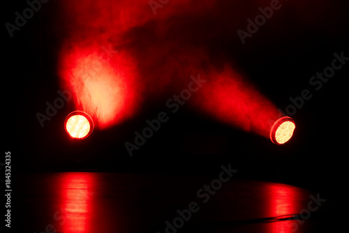 Bright red lights pierce through swirling smoke in a dimly lit space, creating an intense atmosphere during a live performance or event at night.