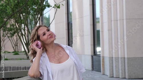 A woman wearing headphones is talking on her cell phone. She is smiling. The phone is pink
