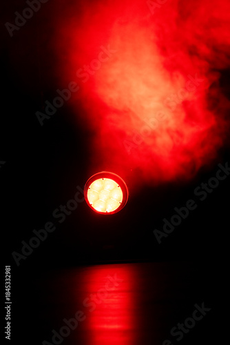 Bright red lights pierce through swirling smoke in a dimly lit space, creating an intense atmosphere during a live performance or event at night.