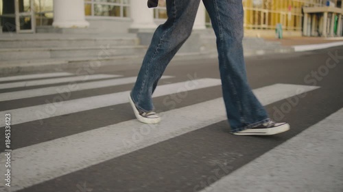 Person walks across a large crosswalk on a city street wearing casual clothes and sneakers on a clear day