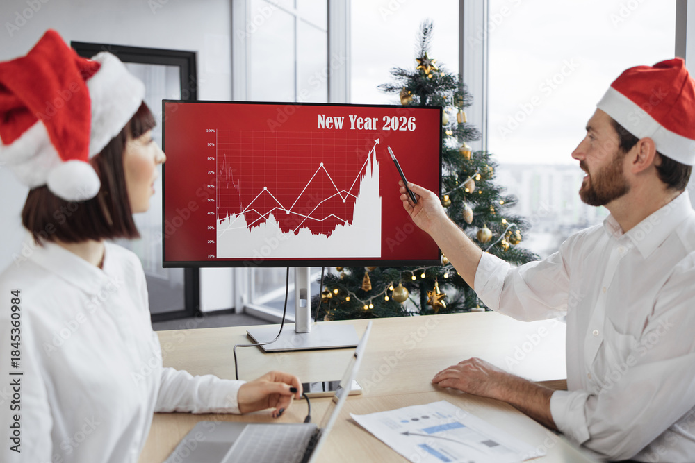 Obraz premium Close up of festive businessman manager in Santa hat sitting near big digital wall screen with company financial and growth charts and talks to multiethnic colleagues discussing results of project.