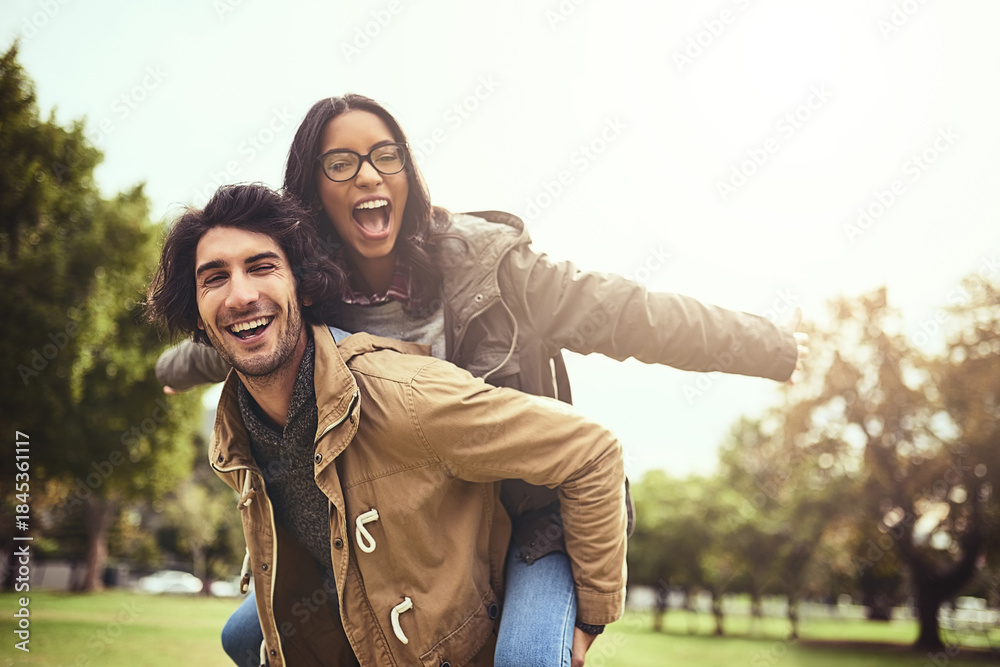 Fototapeta premium Couple, piggy back and fun for portrait in park with care, bonding and adventure in spring on holiday. Interracial love, man and woman with hug, airplane and playful on vacation with game in Toronto