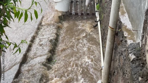 High angle view of muddy flood water overflowing from a small drainage ditch during heavy rain.