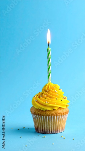 Yellow frosted cupcake with lit green and white candle