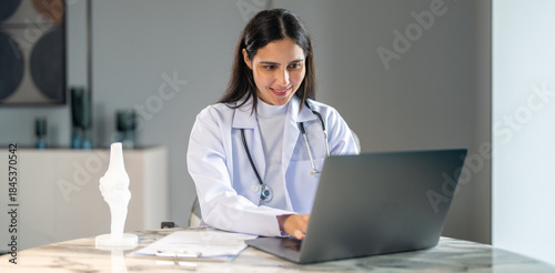 Female doctor use laptop and clipboard work during online medical consultation or telehealth appointment in modern hospital, digital healthcare communication, remote diagnosis and online patient care