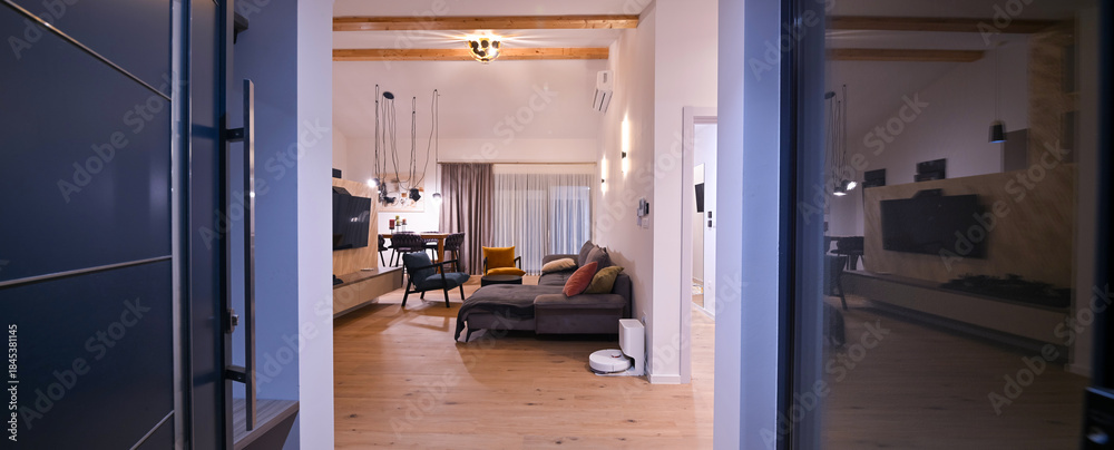 Obraz premium Modern open-plan living and dining area with an integrated kitchen, featuring a comfortable sofa, stylish armchairs, and a bar-height dining table. Wooden floors and ceiling beams enhance this