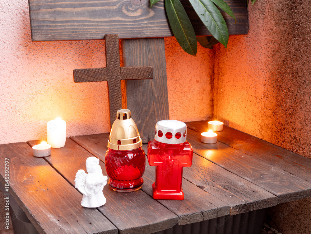 Obraz premium Christian memorial altar with candles, cross, angel figurine, and red grave lamps.
