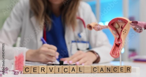 Wooden cubes on table spell words Cervical Cancer while female doctor writes notes. Anatomical uterus model appears to explain gynecology screening
