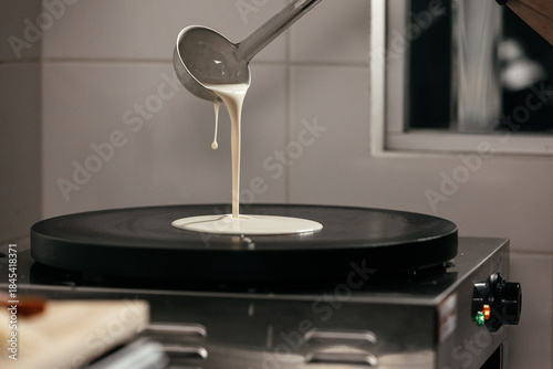 Fotografie Pouring batter from a ladle onto a hot griddle, creating a round pancake shape,