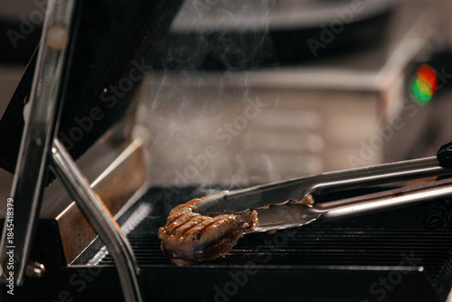 Фотография Grilled meat being flipped with tongs on a hot grill, surrounded by steam and sm