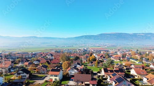 Aerial view of houses and trees in a cityscape bathed in sunlight, with mountains in the distance, Chavornay, Vaud, Switzerland.