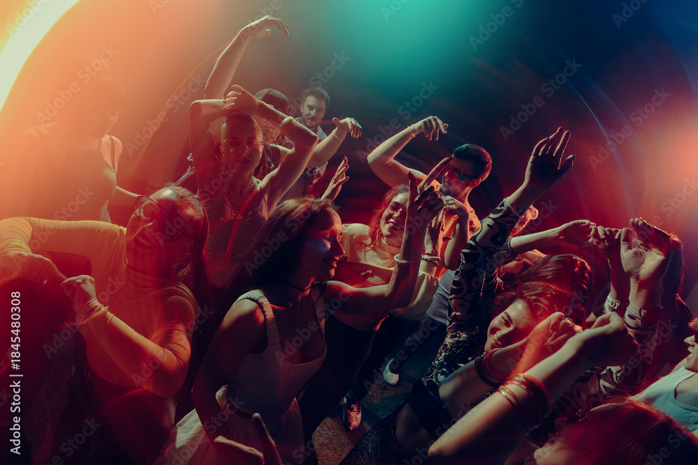 Naklejka premium Joyful crowd dancing under cinematic colorful lights. Concept of collective happiness, emotional expression, night freedom, music driven unity and New Year celebration mood.