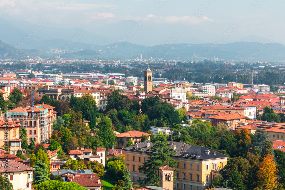 Fototapeta premium Panoramic cityscape of Bergamo with red rooftops, green trees, and clock tower in a European town