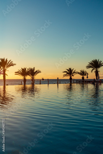 Sunset over infinite pool with palm trees and ocean horizon at a luxury resort