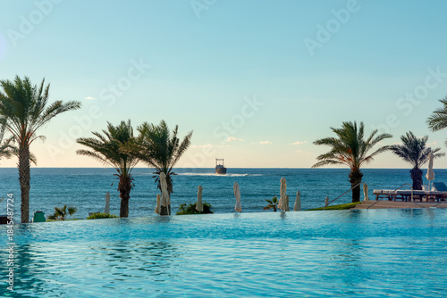 Canvas Print Luxurious oceanfront resort poolside with palm trees overlooking calm sea and sh