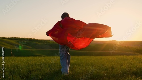 Картината върху платно Superhero little girl in red mantle play against sun sky