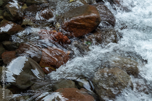 Close up fresh waterfall stream rushing over wet brown river rocks texture in a natural setting.