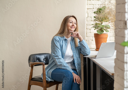Portrait of minded charming woman sit behind desktop arms on cheek look interested window home indoors
