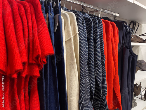 Colorful clothing rack display with red sweaters and patterned shirts in fashion store