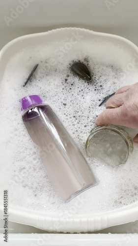 Vertical video social media - Closeup of a hand placing an empty glass jar of marmalade into a bowl of soapy water, next to other items of washing up.